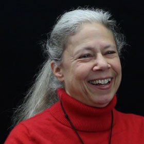 Picture of Sandra Braman. Woman with red sweater smiling with long hair in a ponytail.